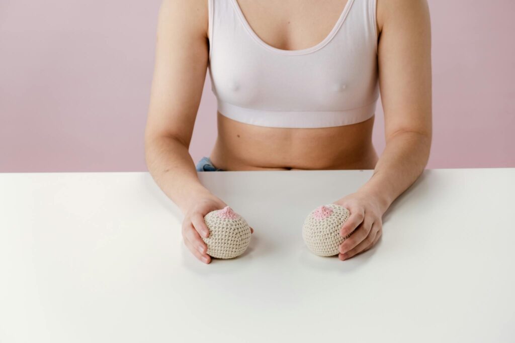 A woman in a sports bra holds knitted breast models on a pink background, symbolizing breast health awareness.