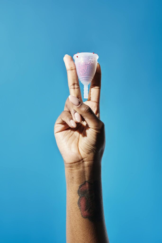 Close-up of a tattooed hand holding a menstrual cup in front of a bright blue background.